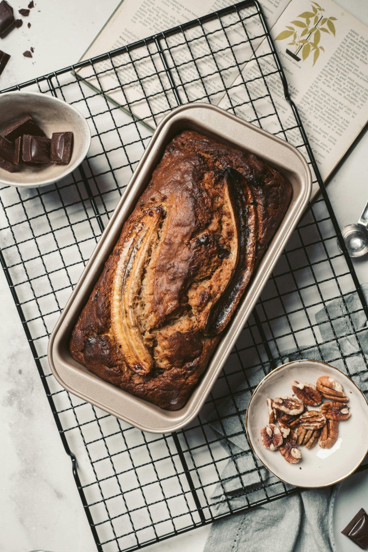 Freshly baked banana bread loaf with a whole banana on top, cooling on a rack.