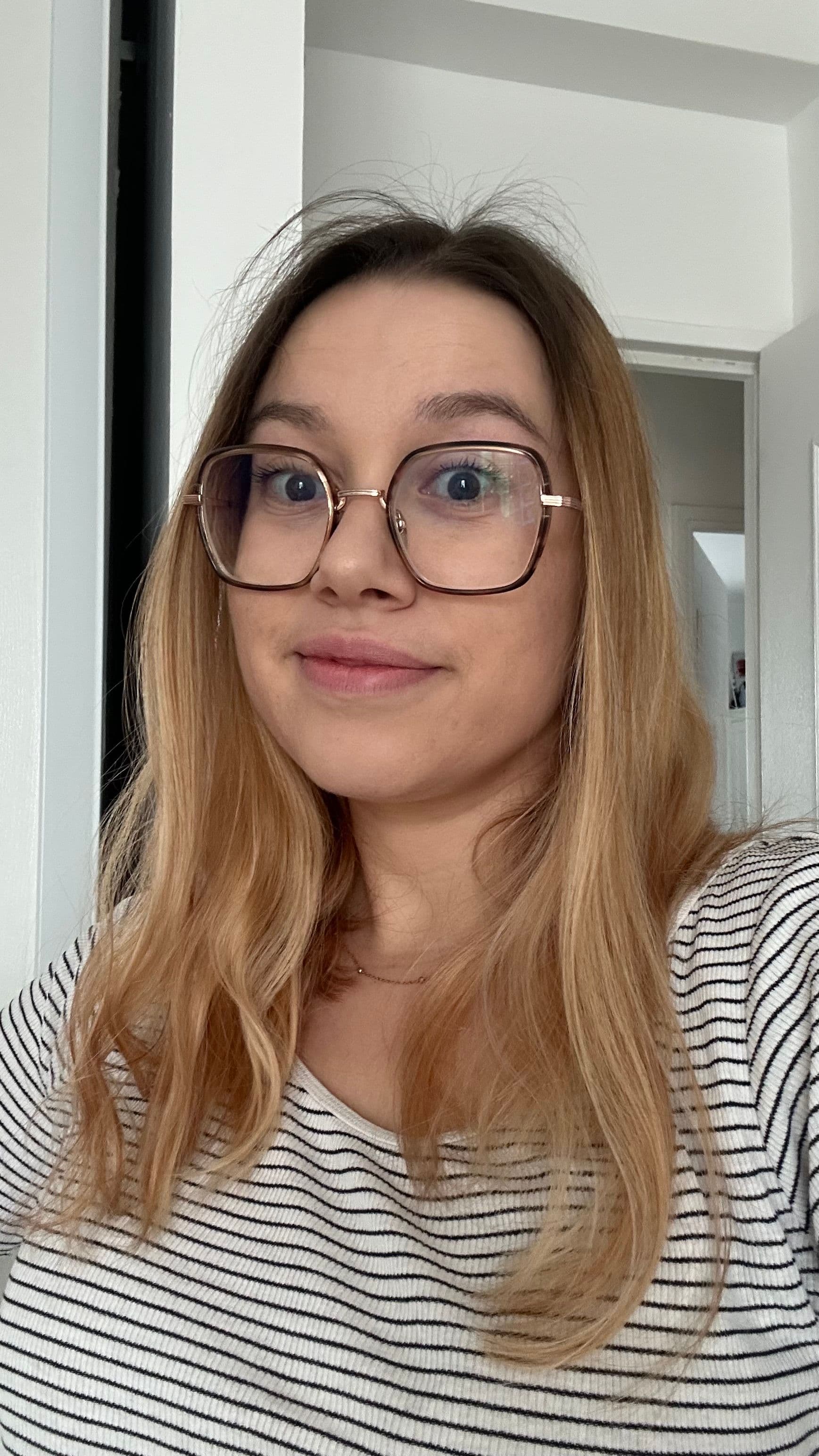 A young woman with light brown hair and glasses smiles directly at the camera.